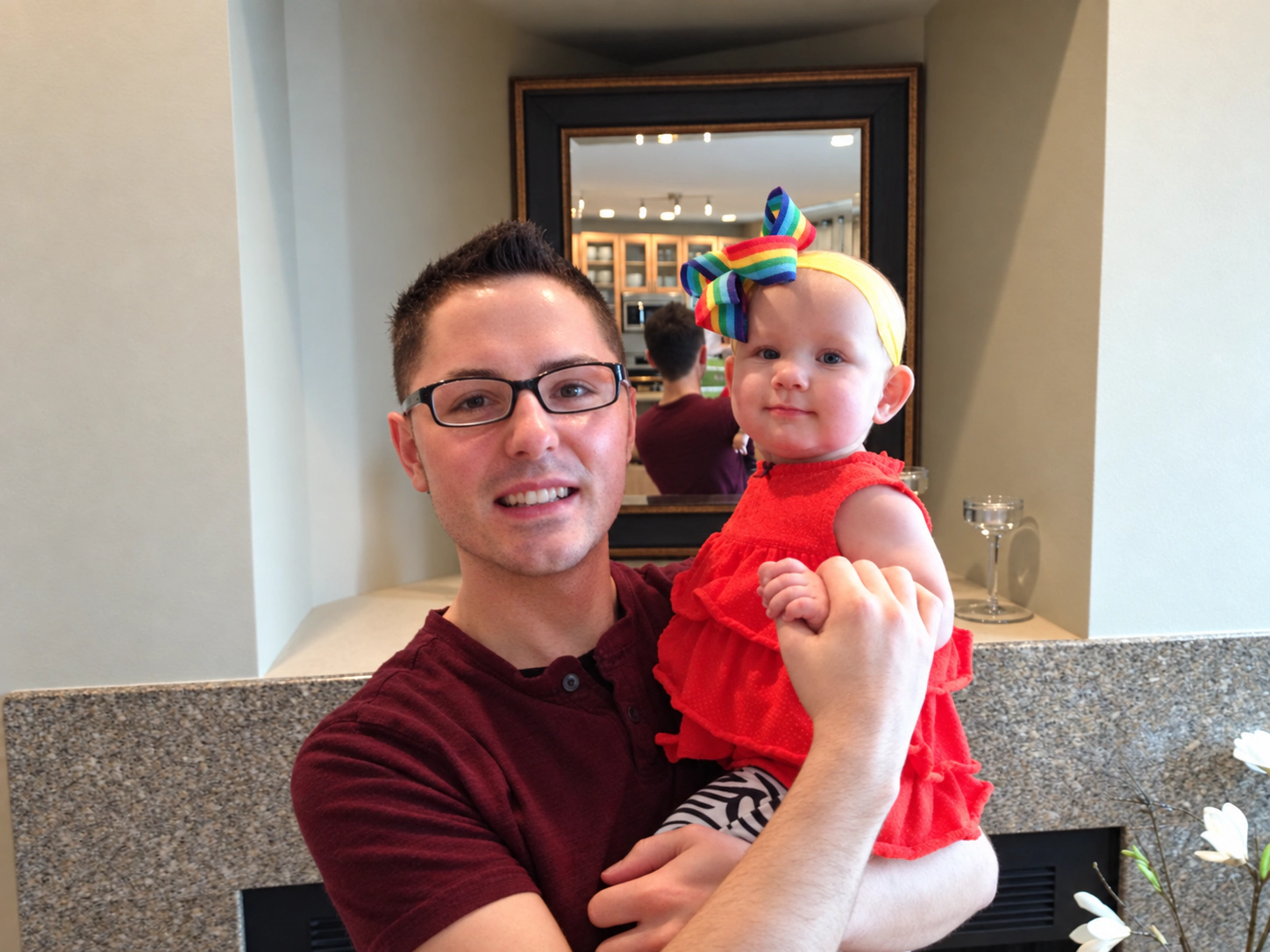 Frank Golden holding Sophia in a red dress and rainbow bow at home.