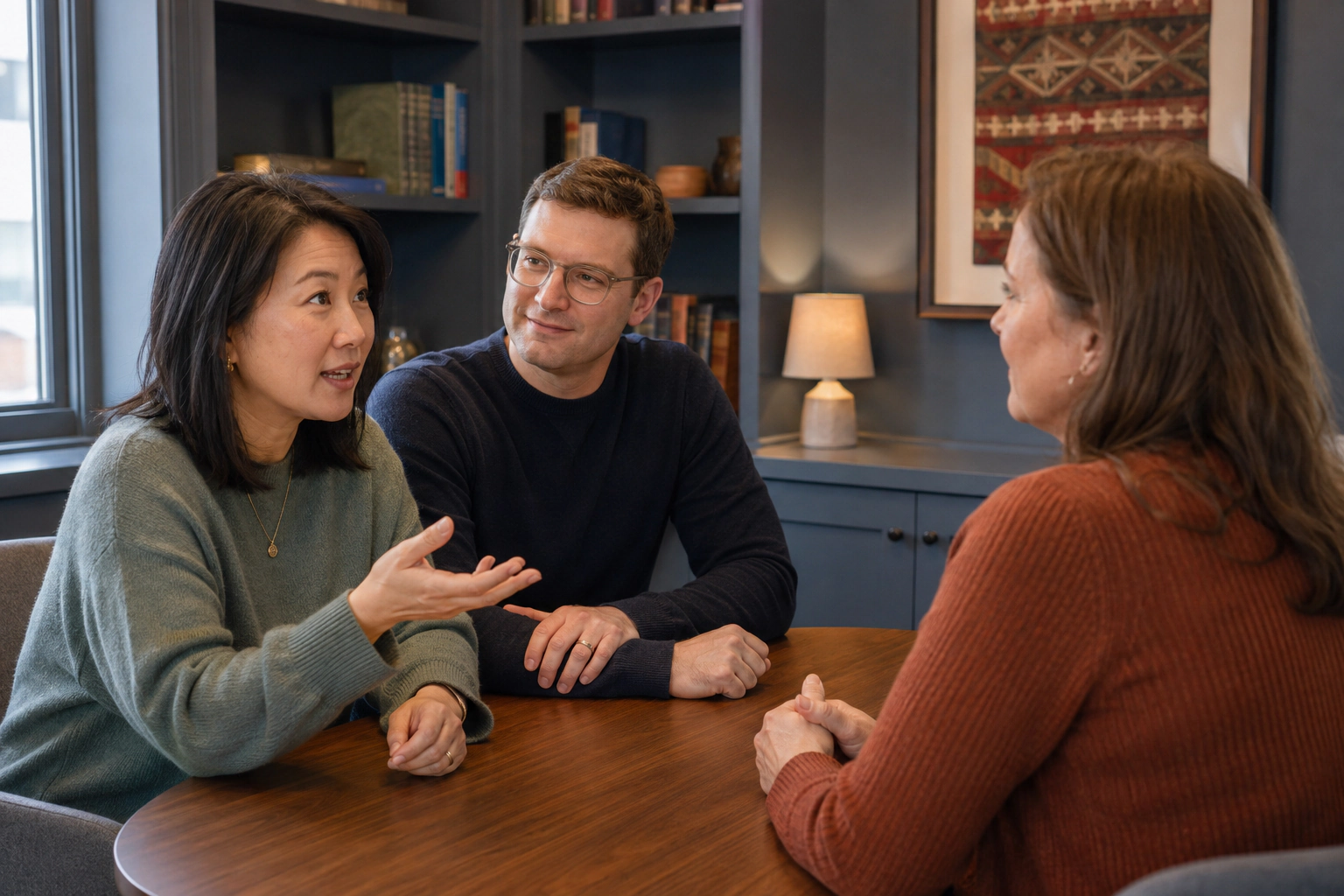 A couple discussing questions with a woman at a wooden table.