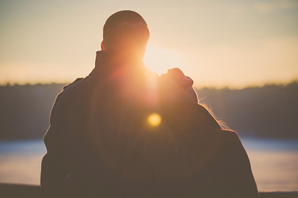 Blog-18-pic couple stands next to each other looking at the sun set between them.