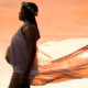Pregnant woman with a flower crown stands in front of the sunset as her dress blows.