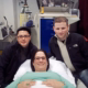 pregnant surrogate smiles on bed between two dads.