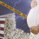 pregnant woman holds her stomach next to spilled popcorn and caution tape on a lightning bolt background.
