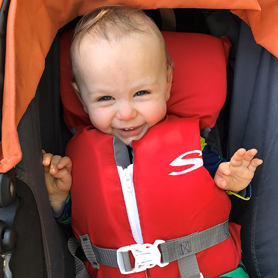 silas young boy sits in stroller with a red life jacket on.