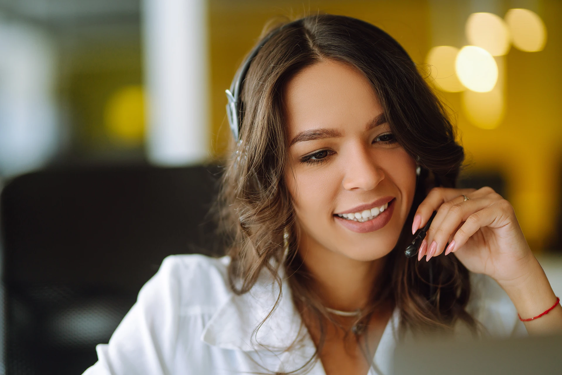 Close-up of woman who is smiling in white shirt talking to a client over a headset.