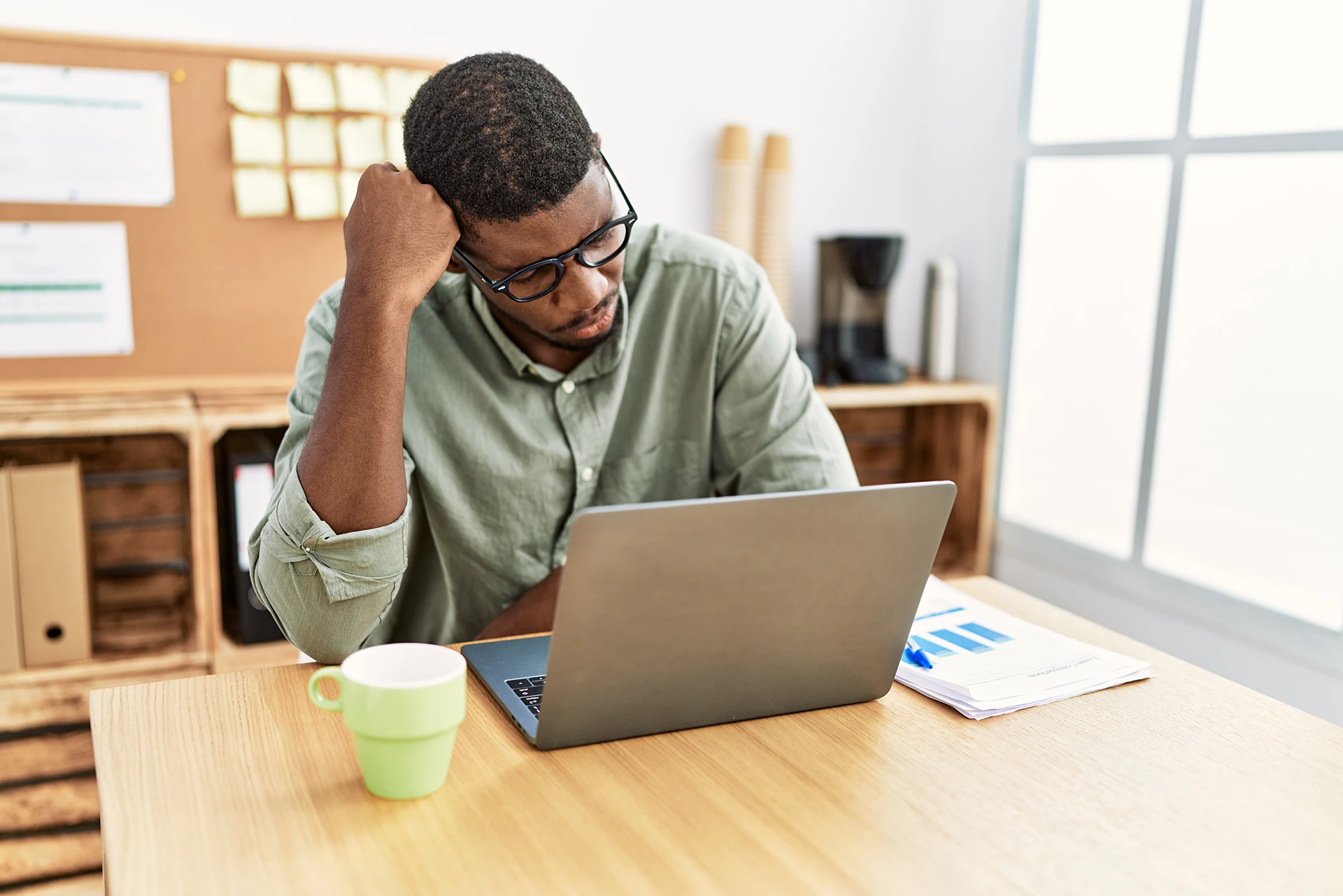 Single Intended Parent in a green button-up rests his head on his hand while he looks confused in front of his open laptop.