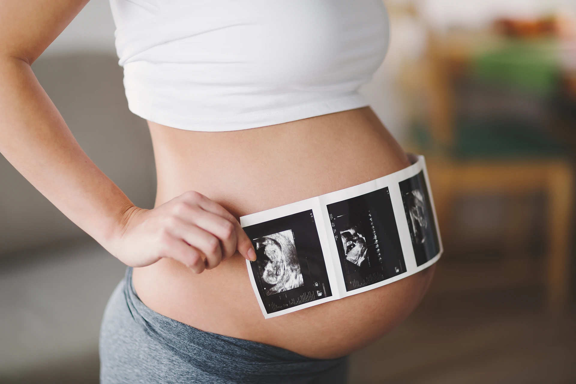 Close-up of a pregnant woman's stomach with ultrasound photos being held against it.