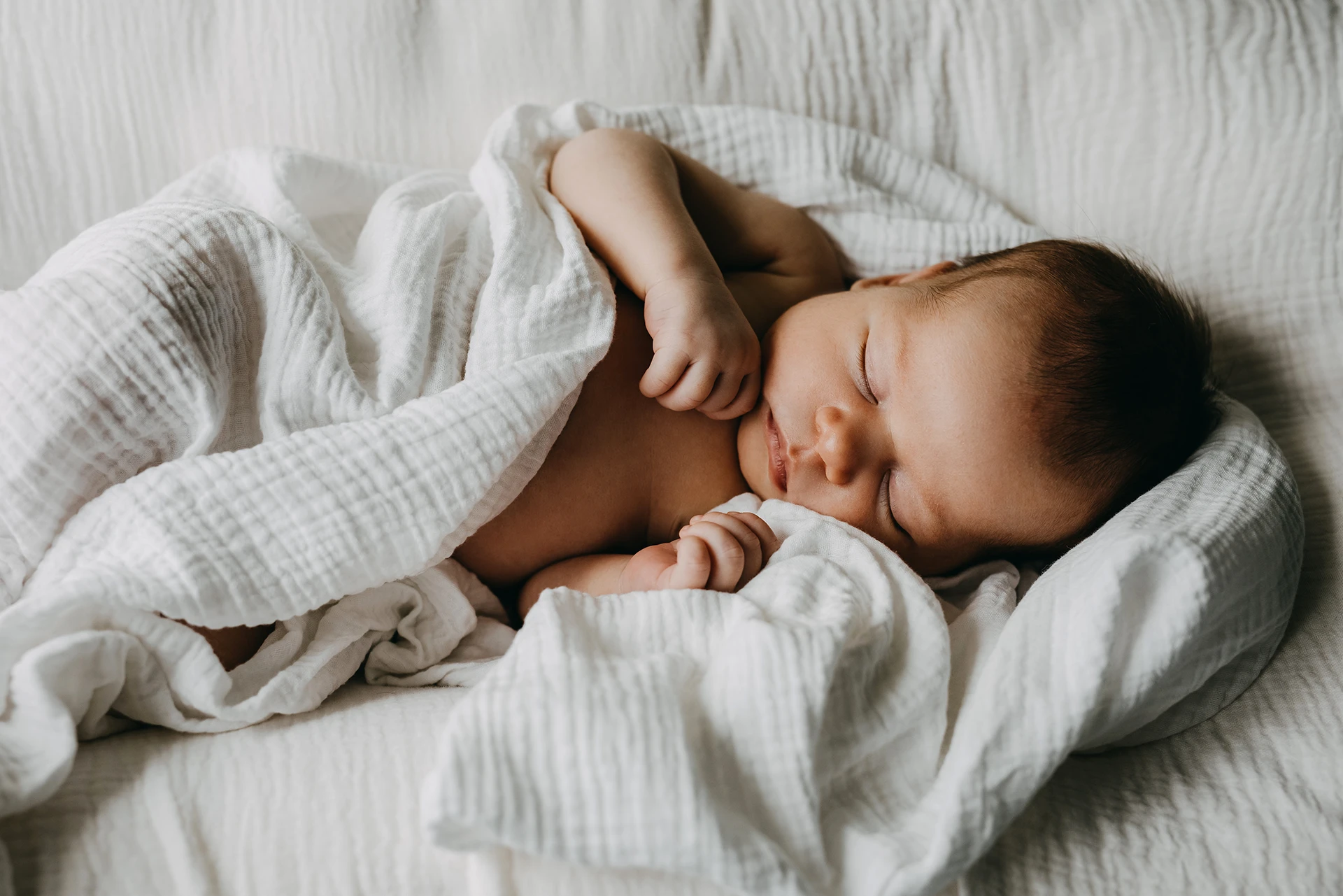 Newborn baby sleeping in a white blanket.