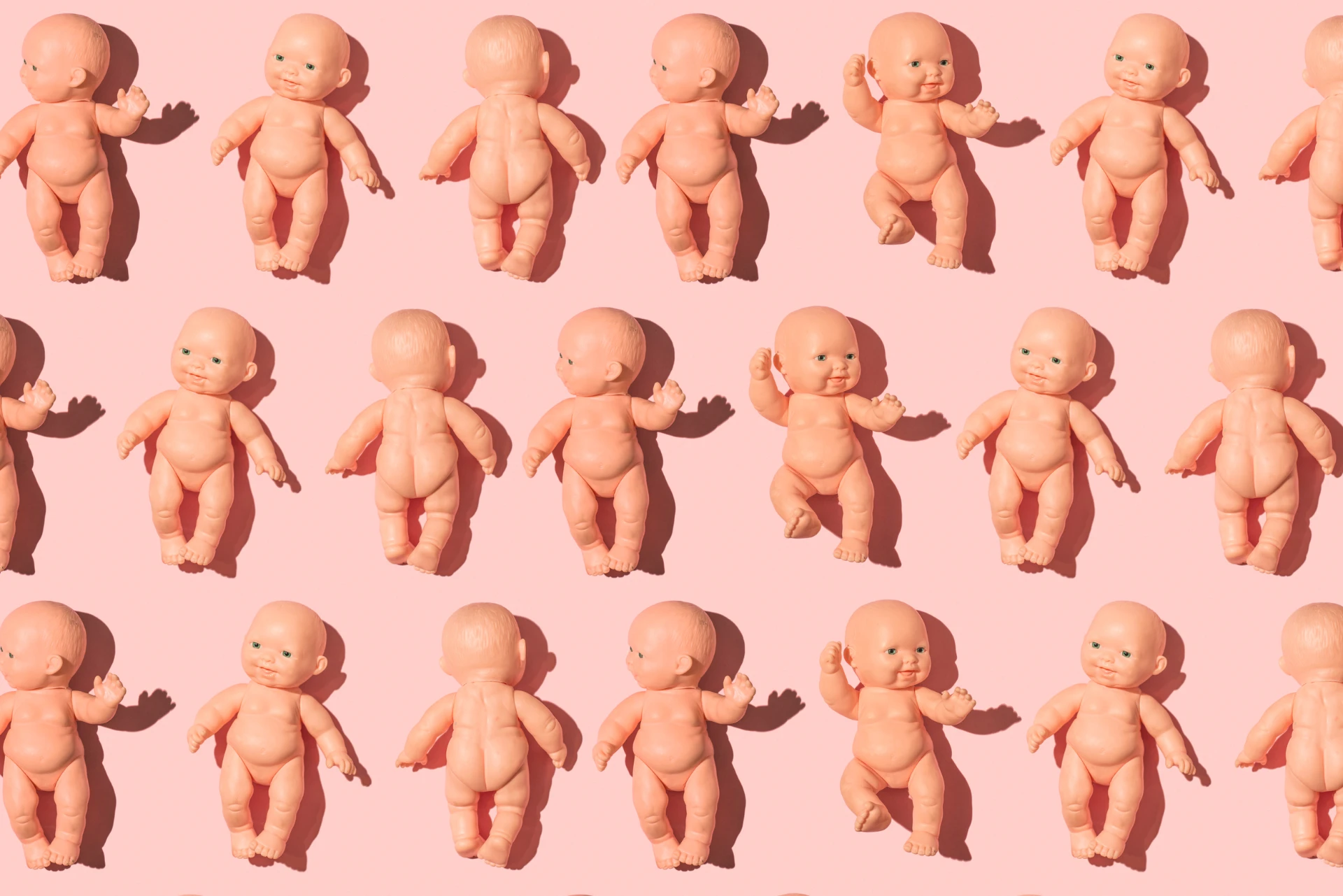 Baby dolls arranged on a pink surface, placed in a neat pattern.