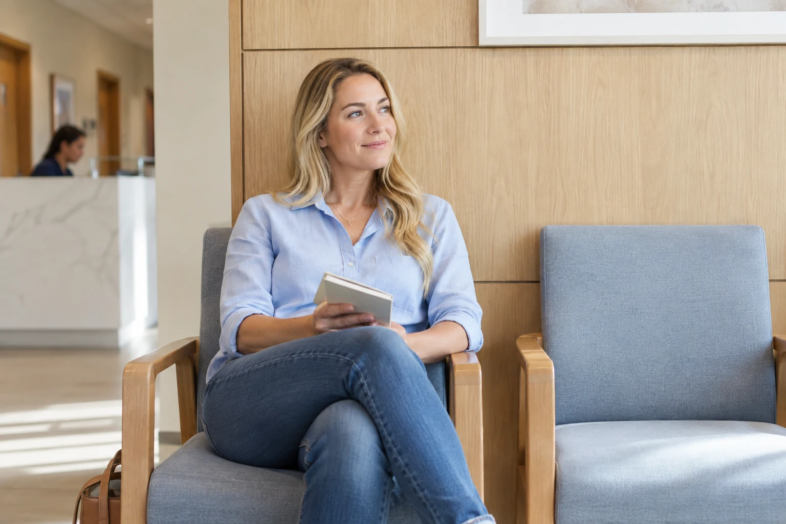 A woman holds a notebook while seated in a clinic waiting area.