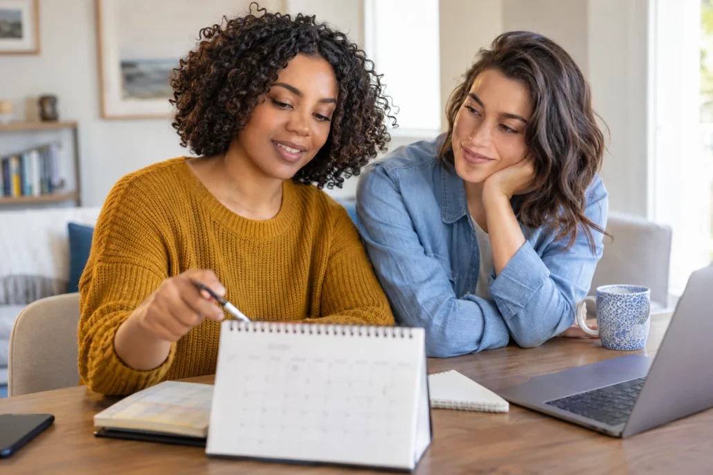 Two women discusses a calendar together at a bright home desk.